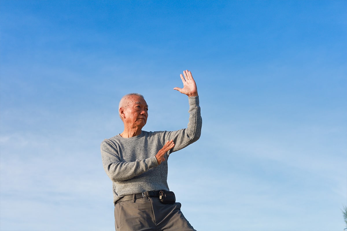 Man with Parkinson's Diseas doing Tia Chia outside during a blue sky day