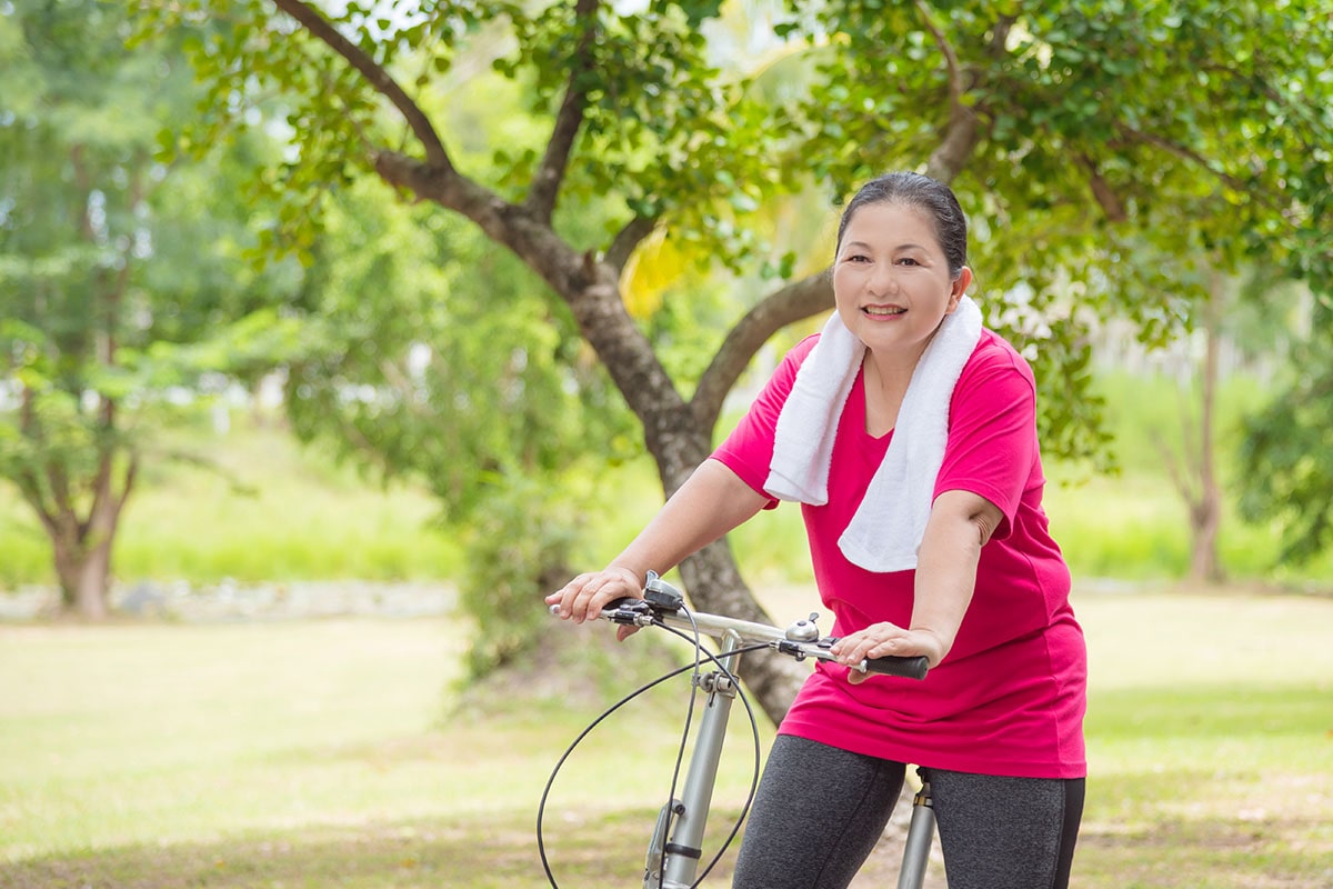 Woman living with parkinson's wearing a red shirt and riding a bike for her outdoor exercise