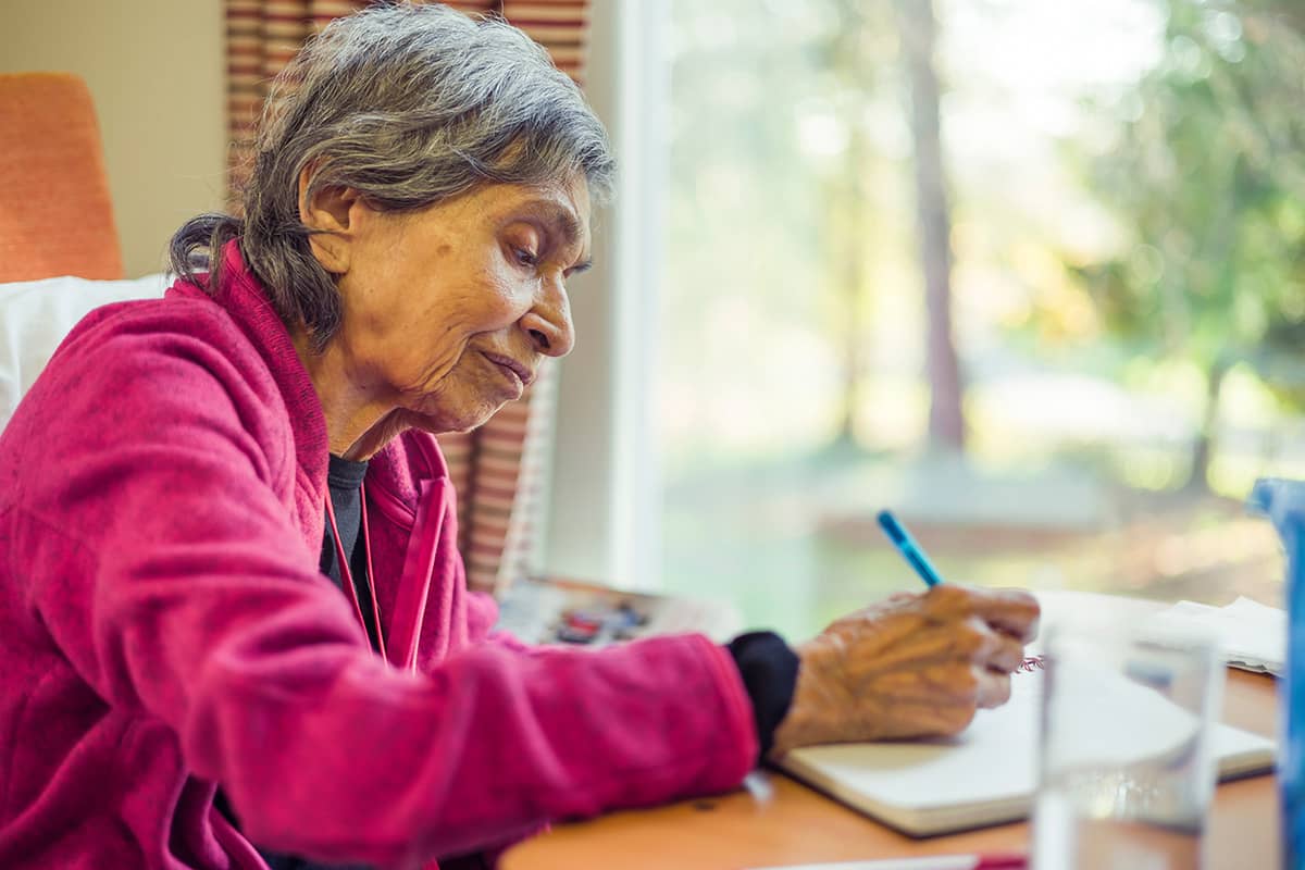 Old Asian Indian woman with Parkinson's Disease writing in journal during the holidays