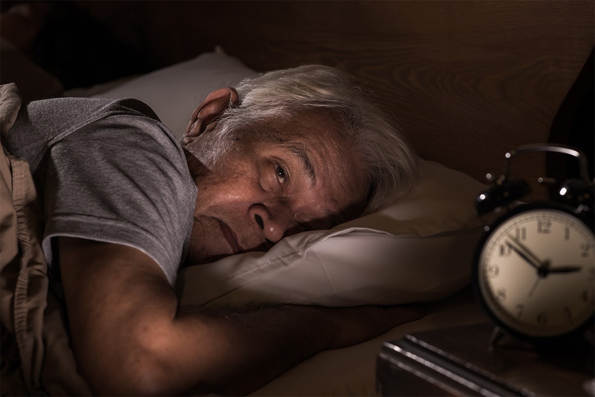 Man with Parkinson's disease laying in bed while staring at his clock
