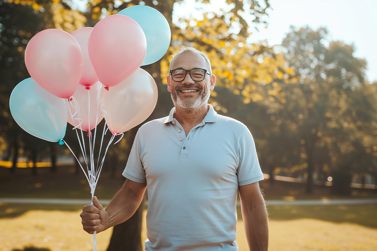 Older man holding balloons smiling